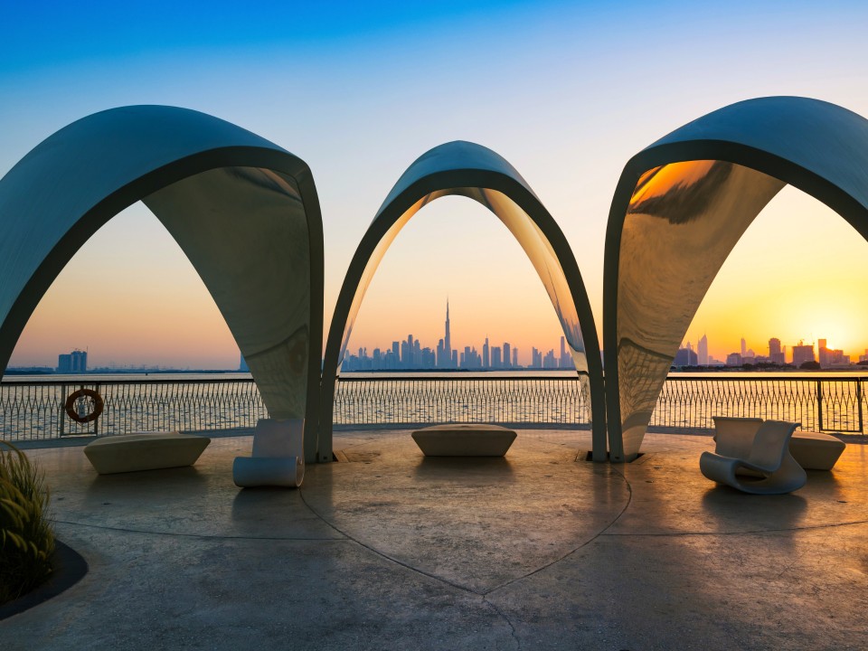 Eine Aussichtsplattform, dahinter Meer und die Skyline von Dubai bei Sonnenuntergang.____