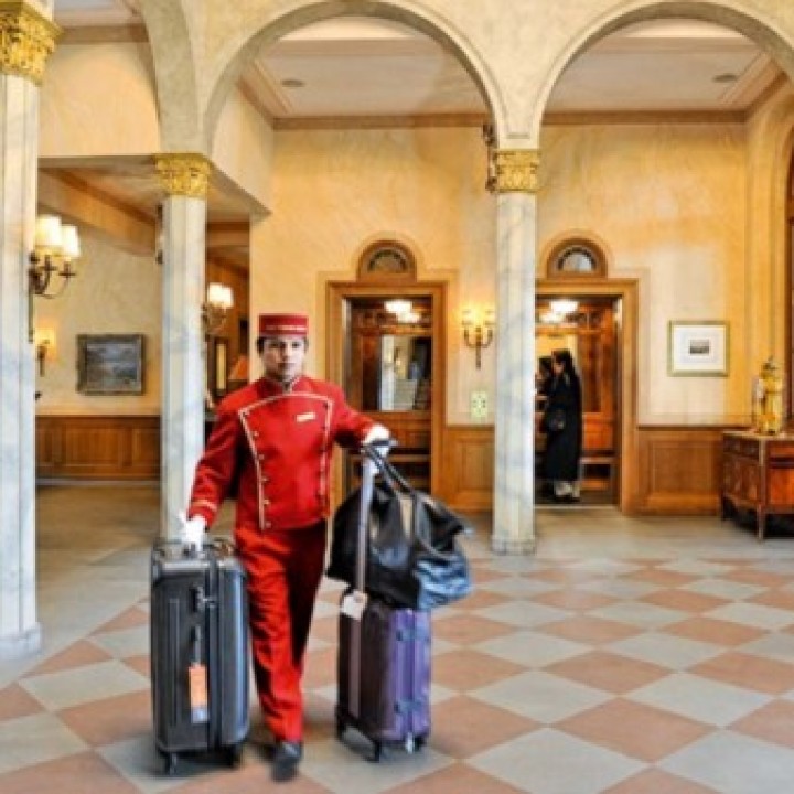 Liftboy in Pagen-Kleidung in einem Foyer und drei Koffern____