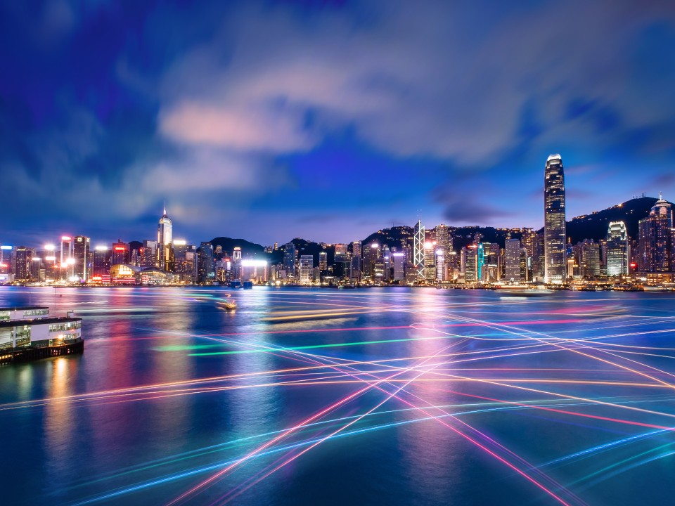 Skyline von Hongkong, davor Meer, bei Nacht. Bunte Laser beleuchten die Gebäude und das Wasser.____